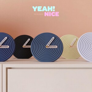 Könnte beinhalten: Eine Sammlung moderner, runder Uhren in verschiedenen Farben, darunter Blau, Schwarz, Gelb und Weiß. Jede Uhr hat ein Spiraldesign und weiße Zeiger. Der Text "YEAH! NICE" und "home decor" ist im Bild enthalten.