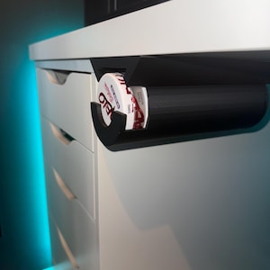 Peut inclure: Un support noir imprimé en 3D monté sous un bureau blanc, tenant une boîte de tabac à priser Copenhagen Wintergreen Long Cut.