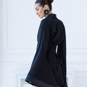 May include: A black wrap dress with long, wide sleeves and a satin trim. The dress has a tie at the waist and a slightly asymmetrical hemline.