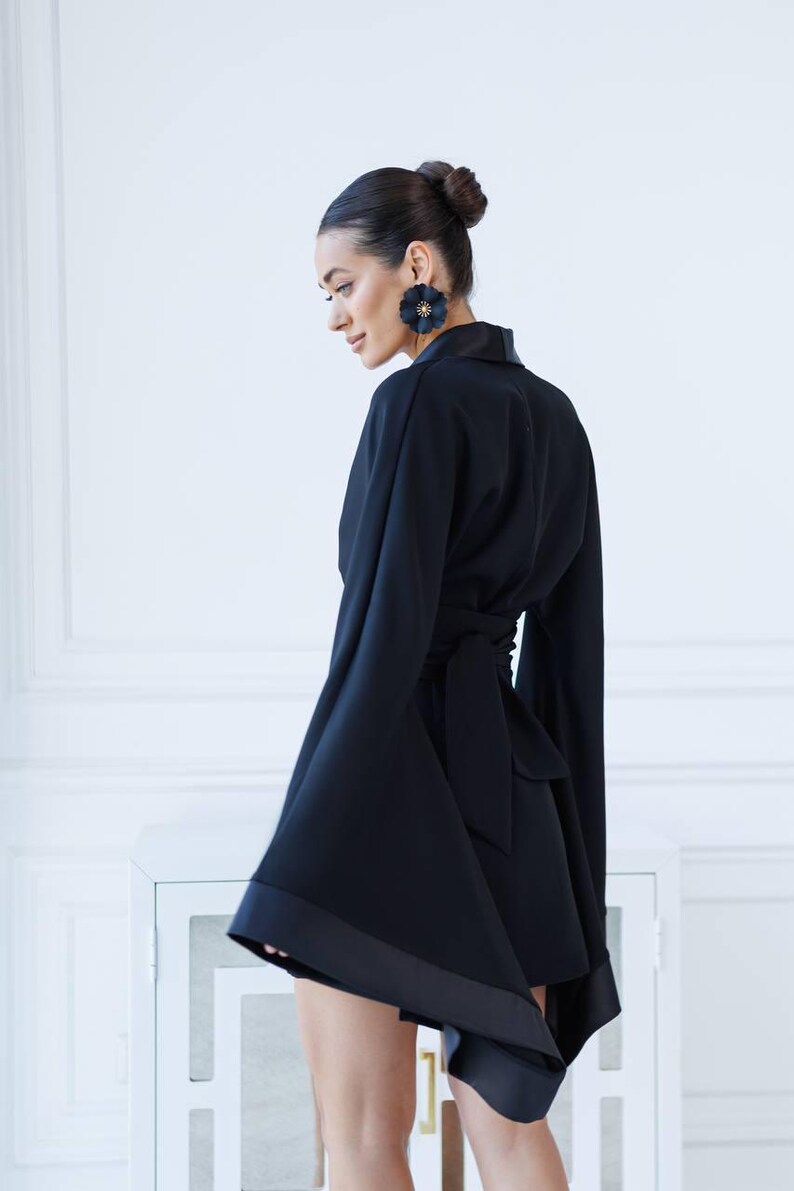 May include: A black wrap dress with long, wide sleeves and a satin trim. The dress has a tie at the waist and a slightly asymmetrical hemline.
