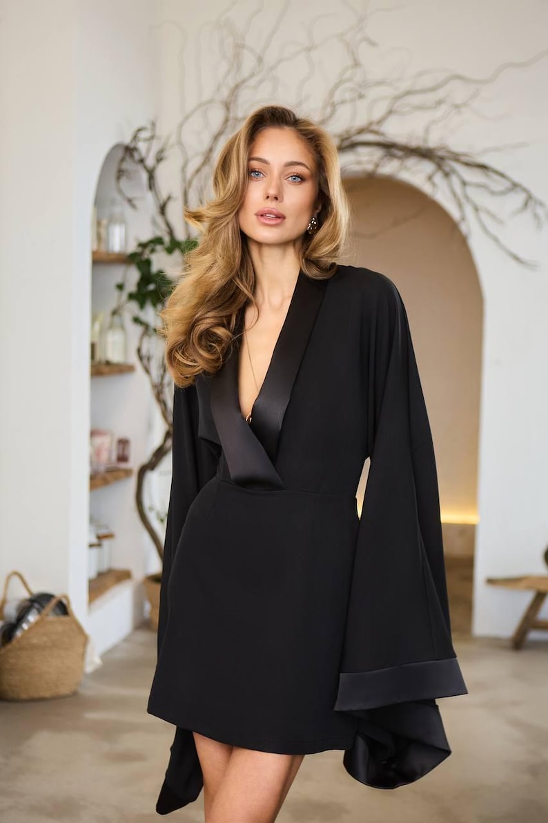 May include: A black mini dress with a satin collar and long sleeves. The sleeves have wide cuffs with a satin trim.