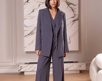 May include: A woman wearing a gray suit with a blazer and wide-leg pants. The suit is a solid color and has a classic, tailored fit.