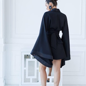 May include: A black short-sleeved dress with a wrap-style waist and wide, flowing sleeves. The dress is worn by a person with their back to the camera. The person is wearing black high heels.