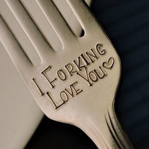 Op de afbeelding: Een zilveren vork met de woorden "I Forking Love You" gegraveerd op het handvat. De vork ligt op een wit bord.