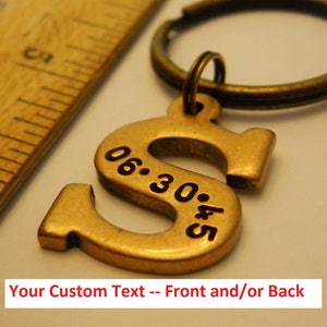 May include: Gold-toned metal keychain with a letter 'S' charm. The charm has the date '06.30.45' engraved on it. The keychain is attached to a metal ring.