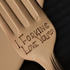 May include: A silver fork with the words "I Forking Love You" engraved on the handle. The fork is resting on a white surface.