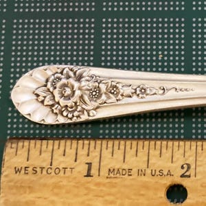 May include: A silver-plated fork with an ornate floral design. The fork is approximately 7 inches long and has the words "Made in U.S.A." stamped on the back.