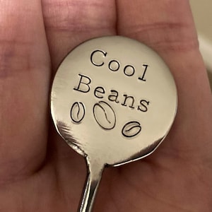 May include: A silver stirring spoon with a round handle that says "Cool Beans" with three coffee bean icons.