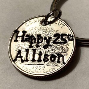 May include: A silver quarter coin keychain with the words "Happy 25th Allison" cut out. The coin is from 1999 and features a tree design. A silver key ring is attached to the coin.