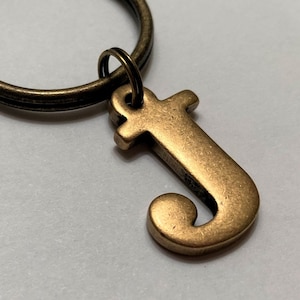 May include: A gold-toned letter J keychain charm attached to a bronze-colored key ring.
