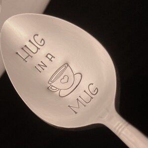 May include: A silver spoon with the words "HUG IN A MUG" engraved on it. A small heart is inside the mug graphic.