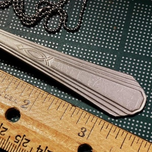May include: A silver spoon necklace with a chain and a fish symbol engraved on the spoon. The spoon is about 3 inches long.