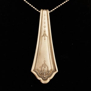 May include: A silver necklace with a pendant made from a vintage silverware piece. The pendant is shaped like a long, narrow teardrop with an ornate design.