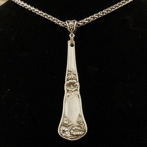 May include: A silver necklace with a long, ornate pendant made from a vintage spoon. The pendant features a floral design.