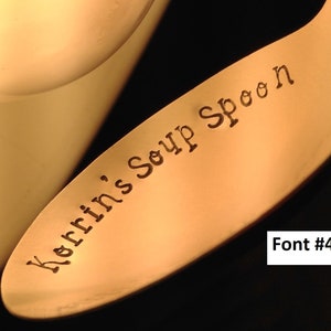 May include: Close-up of a gold-colored soup spoon with the words "Kerrins Soup Spoon" engraved on the handle. The font is a simple, elegant script.