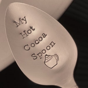 Puede incluir: Una cuchara de plata con las palabras "My Hot Cocoa Spoon" grabadas. También hay un pequeño gráfico de una taza de chocolate caliente con crema batida grabado en la cuchara.