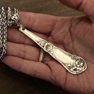 May include: A silver spoon necklace with a floral design. The spoon is attached to a silver chain.