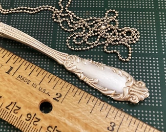 May include: A silver spoon necklace with a ball chain. The spoon is about 2 inches long and has an ornate design. The chain is about 18 inches long.
