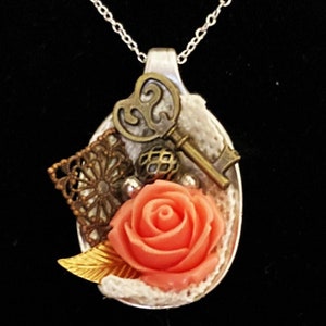 May include: A silver spoon necklace with a pink rose, a key, and other decorative elements.