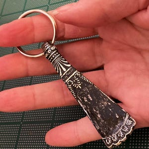 May include: A silver key chain with a decorative black and white design. The key chain is shaped like a small shoe horn.