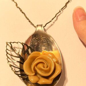 May include: A silver spoon necklace with a gold leaf and a caramel-colored rose pendant.