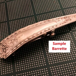 May include: Silver barrette with decorative scrollwork and a hinged clasp. The rectangular barrette has an ornate design along the edges. The text "Sample Barrette" is in a white box.