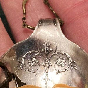 May include: A silver spoon with an ornate floral design, transformed into a pendant with a gold chain.
