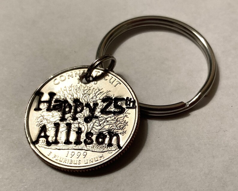 May include: A silver quarter coin keychain with the words "Happy 25th Allison" cut out. The coin is from 1999 and features a tree design. A silver key ring is attached to the coin.