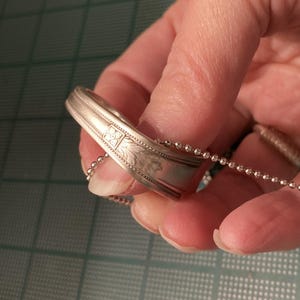 May include: A silver spoon ring with a floral design and a silver chain attached to it.