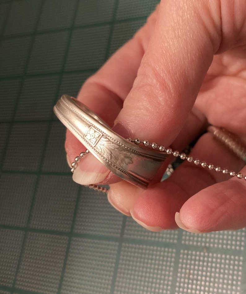 May include: A silver spoon ring with a floral design and a silver chain attached to it.