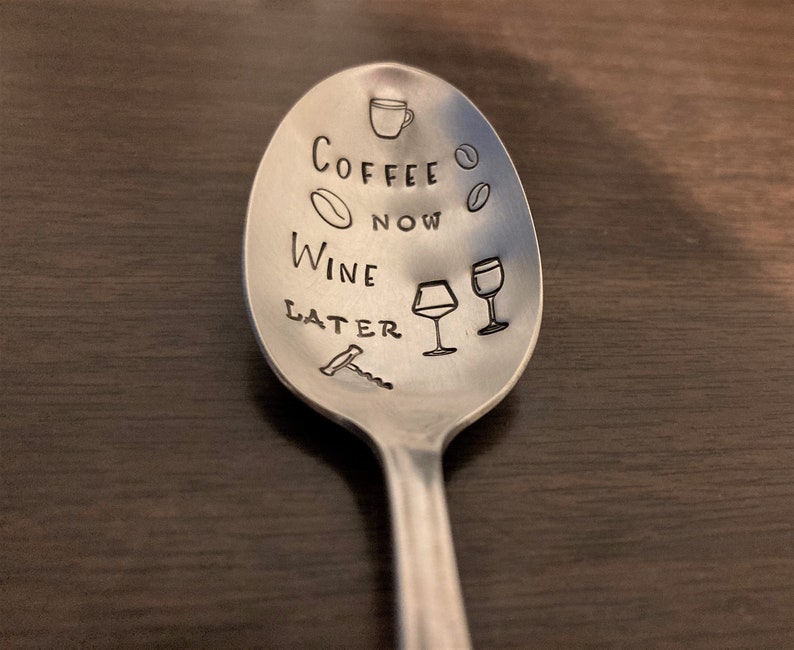May include: A silver spoon with the text "Coffee Now Wine Later" engraved on it. The spoon also has a coffee cup, coffee bean, wine glass, and corkscrew engraved on it.