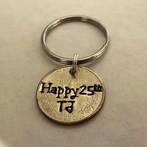 May include: A silver keychain with a quarter coin pendant. The coin is engraved with "Happy 25th" and "TJ" along with the year 2000. The keychain has a silver ring.