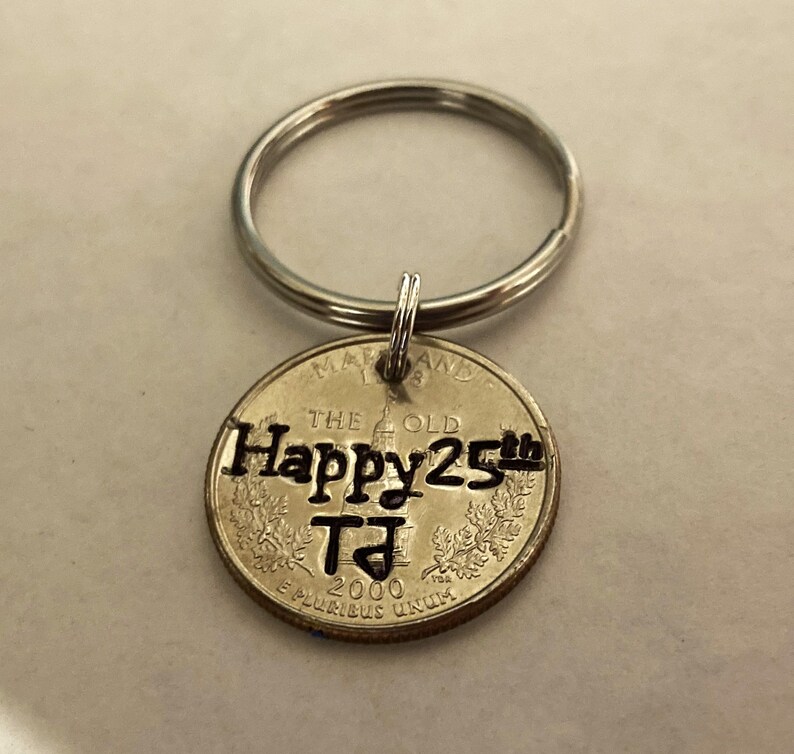 May include: A silver keychain with a quarter coin pendant. The coin is engraved with "Happy 25th" and "TJ" along with the year 2000. The keychain has a silver ring.
