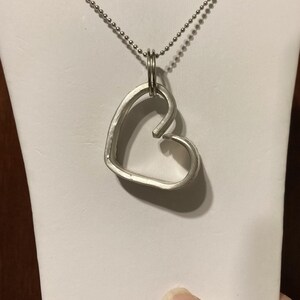 May include: A silver heart-shaped pendant necklace with a ball chain. The pendant is made of a single piece of metal that is bent into a heart shape.