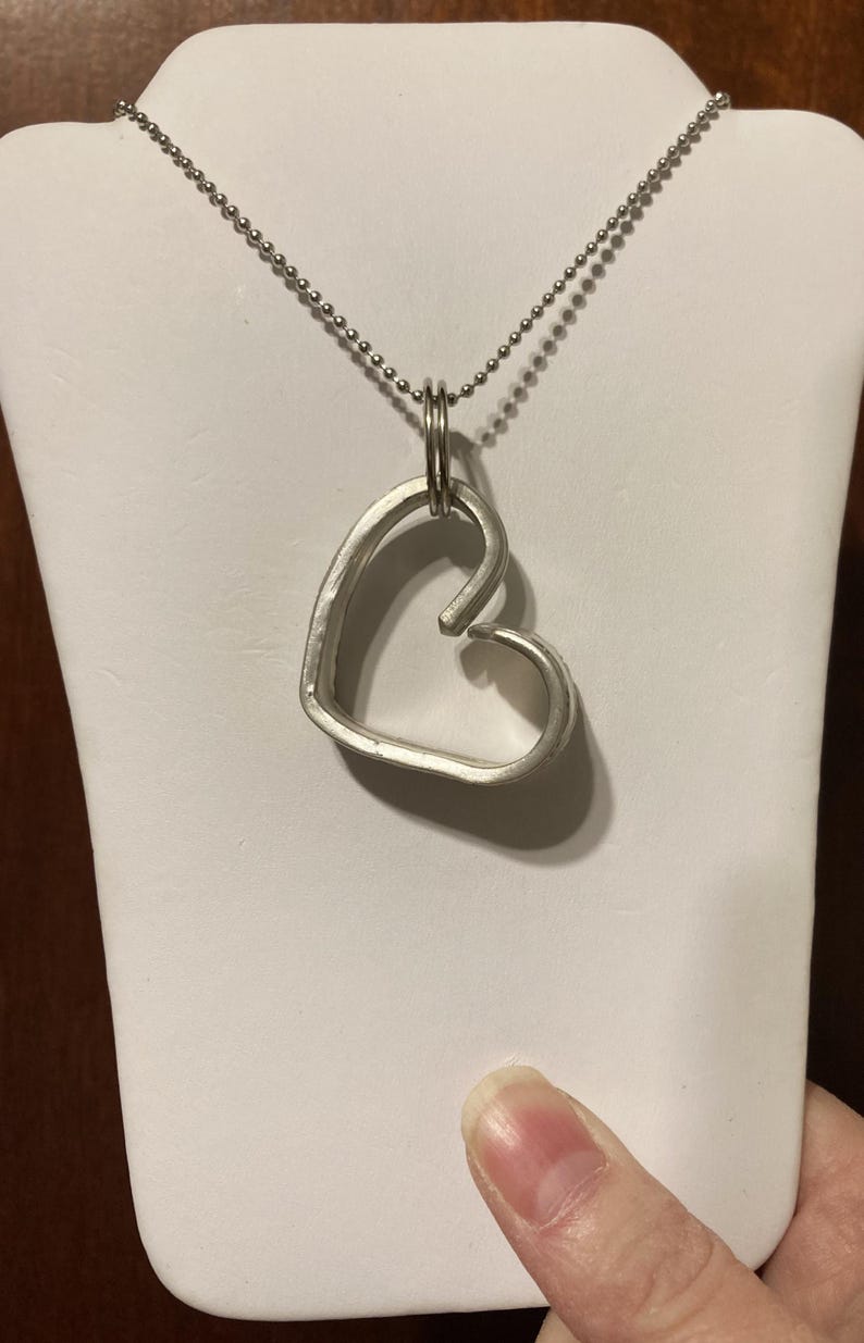 May include: A silver heart-shaped pendant necklace with a ball chain. The pendant is made of a single piece of metal that is bent into a heart shape.