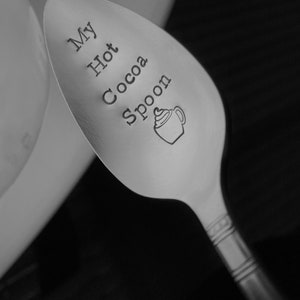 May include: A silver spoon with the words "My Hot Cocoa Spoon" engraved on it. The spoon has a decorative design on the handle.