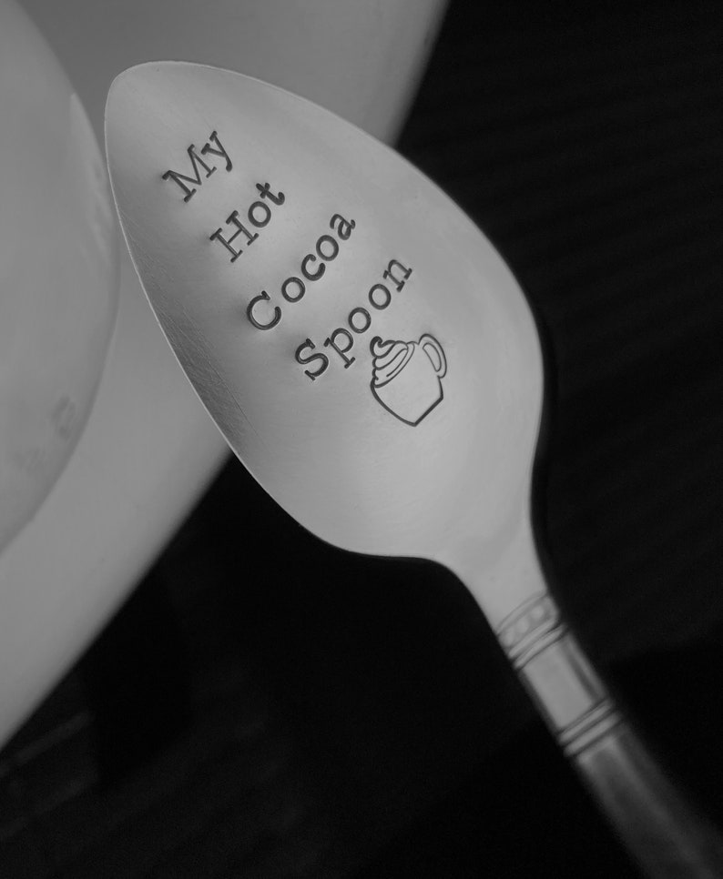 May include: A silver spoon with the words "My Hot Cocoa Spoon" engraved on it. The spoon has a decorative design on the handle.