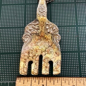 May include: A silver fork necklace with a decorative handle and tarnished finish. The fork is about 1 inch long. The necklace is made of a silver chain.