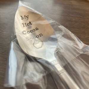 May include: A silver spoon with the words "My Hot Cocoa Spoon" engraved on it. A small illustration of a mug of hot cocoa with whipped cream is also engraved on the spoon.