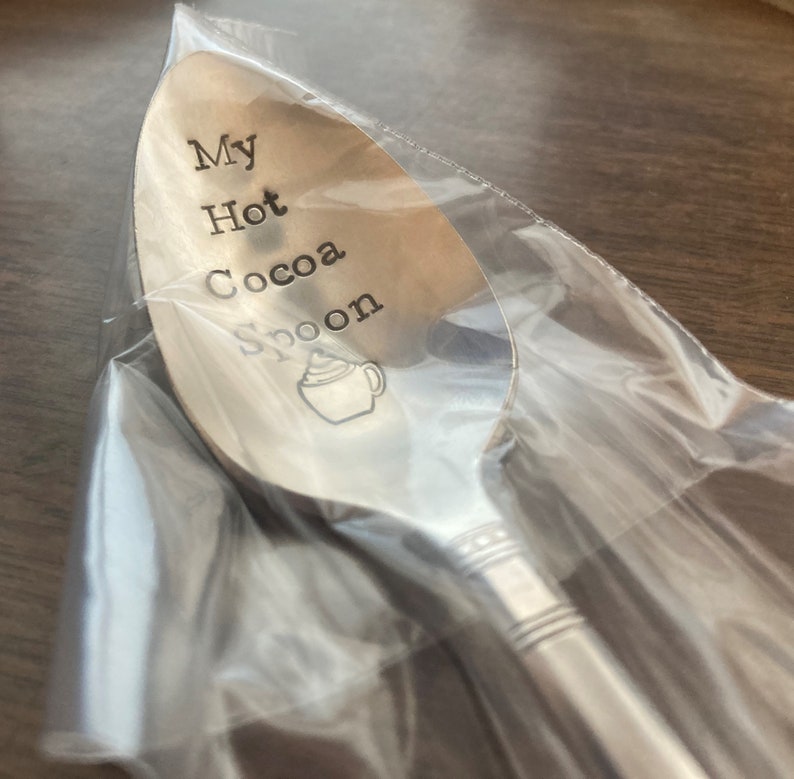 May include: A silver spoon with the words "My Hot Cocoa Spoon" engraved on it. A small illustration of a mug of hot cocoa with whipped cream is also engraved on the spoon.