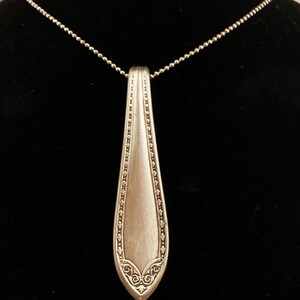 May include: A silver necklace with a pendant made from a vintage silverware spoon. The spoon has an ornate design and is attached to a silver chain.