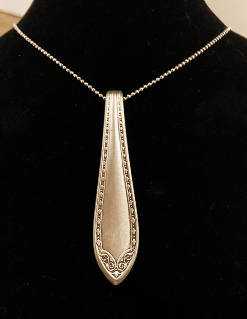 May include: A silver necklace with a pendant made from a vintage silverware spoon. The spoon has an ornate design and is attached to a silver chain.