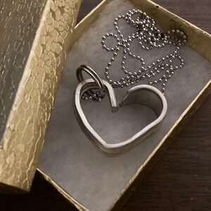 May include: A silver heart-shaped pendant necklace with a silver chain in a gold gift box.