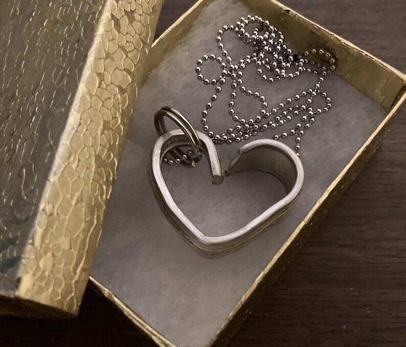 May include: A silver heart-shaped pendant necklace with a silver chain in a gold gift box.