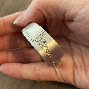 Puede incluir: Un brazalete de plata hecho de una cuchara reutilizada con un dise&ntilde;o floral adornado.