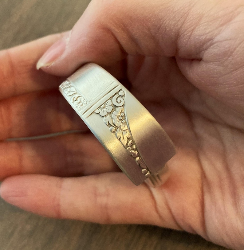 Puede incluir: Un brazalete de plata hecho de una cuchara reutilizada con un dise&ntilde;o floral adornado.