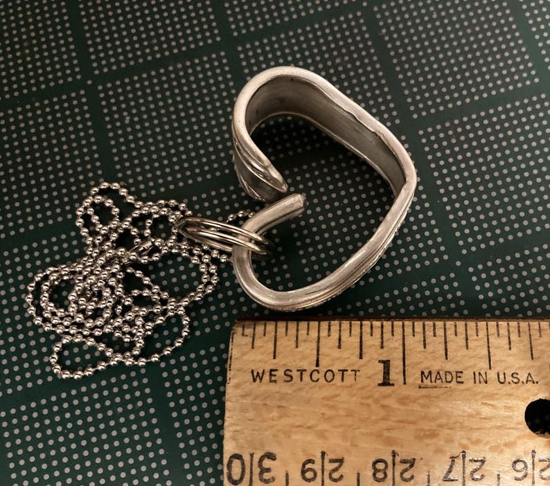 May include: A silver heart-shaped pendant necklace made from a repurposed spoon. The necklace is approximately 1 inch in length and features a silver ball chain.