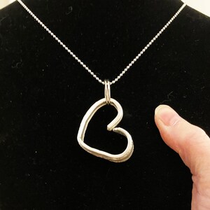 May include: A silver necklace with a heart-shaped pendant. The pendant is made of thick, twisted wire and has a textured surface.