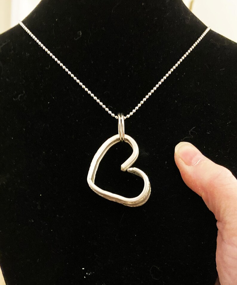 May include: A silver necklace with a heart-shaped pendant. The pendant is made of thick, twisted wire and has a textured surface.