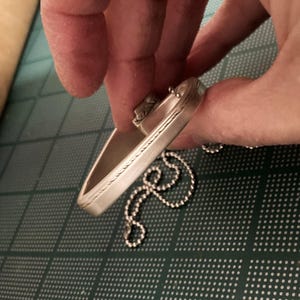 May include: A silver bracelet with a decorative design and a chain attached.